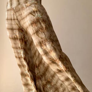 May include: Flowing, wide-leg pants in shades of brown with a tie-dye effect. The pants feature embroidered floral details in soft pastel colors. The fabric appears lightweight and suitable for warm weather.