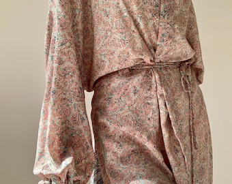 May include: A flowing, patterned robe in shades of pink, teal, and cream. The robe features a V-neck, long sleeves with gathered cuffs, and a matching tie belt. The fabric has a delicate floral design, creating an elegant and bohemian aesthetic.