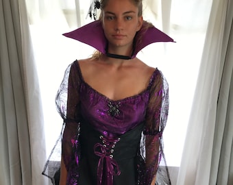 May include: A purple and black costume dress featuring a metallic purple bodice with a black lace overlay, sheer long sleeves, a black corset-style waist with ribbon lacing, a high purple collar, and a small black spider accent on the chest.