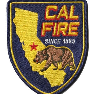 Può includere: Toppa ricamata con la scritta "CAL FIRE" in rosso e giallo, e "SINCE 1885" sotto. La toppa include un contorno giallo della California, una stella rossa e un orso marrone. Lo sfondo è blu navy.