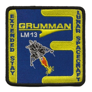 May include: A yellow and blue embroidered patch with the text "Grumman Lunar Spacecraft Extended Stay LM13" and a black and white illustration of a lunar module taking off.