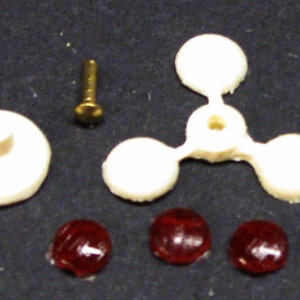 Puede incluir: Un conjunto de piezas de coche de juguete de plástico blanco, que incluye una base, un conector de tres puntas y tres piezas redondas. También hay tres piezas de plástico rojo.