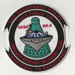 May include: A white, black, and red embroidered patch with the text "USS KEARSARGE CVS-33 TASK FORCE 130" in a circle around a stylized image of a rocket ship and the text "NASA MA-8 PROJECT MERCURY RECOVERY TEAM CANAVERAL TO KEARSARGE".