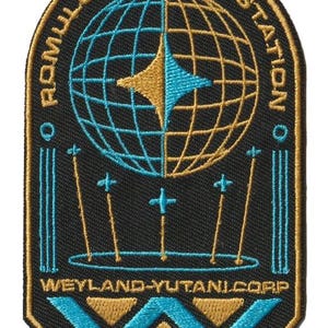 以下が含まれることがあります： 「ROMULUS/REMUS STATION」と「WEYLAND-YUTANI CORP RESEARCH DIVISION」の文字が入った刺繍パッチ。金と青のスターバーストが中央にある地球のデザインで、黒地に金と青のアクセントが施されています。