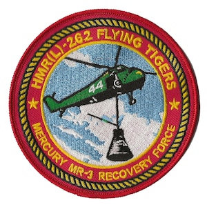 May include: A red, yellow, and white embroidered patch with a helicopter and a capsule. The text on the patch reads "HMR(L)-262 FLYING TIGERS MERCURY MR-3 RECOVERY FORCE".