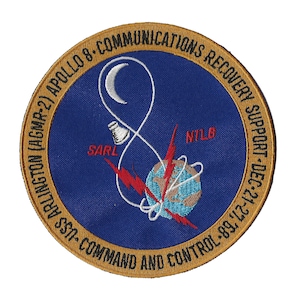 May include: A blue and gold embroidered patch with the text "APOLLO 8-COMMUNICATIONS RECOVERY SUPPORT-DEC-21-ARLINGTON (AGMR-2) SSA-COMMAND AND CONTROL-89,'" and a white crescent moon, a white cord, a red lightning bolt, and a brown and blue globe.