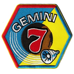 Op de afbeelding: Geborduurde patch in een zeshoekige vorm met een rood, blauw en geel kleurenschema. De patch toont het woord "GEMINI" in wit, het nummer "7" in rood en een gestileerde illustratie van een telescoop. De patch is waarschijnlijk een herdenkingsartikel.