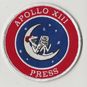 May include: A white, red, and blue embroidered patch with the text "APOLLO XIII PRESS" and a cartoon of a person reading a book on a crescent moon.