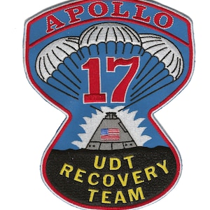 Puede incluir: Un parche bordado azul y negro con el texto "APOLLO 17 UDT RECOVERY TEAM" y una representación de una nave espacial con un paracaídas.