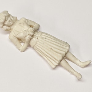 Könnte beinhalten: Weiße Plastikfigur einer Frau, die einen Rock und eine Jacke trägt. Sie hält einen kleinen Blumenstrauß in der Hand.