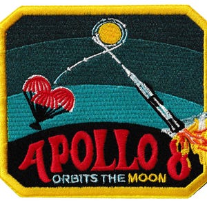Könnte beinhalten: Gestickter Aufnäher mit der Apollo 8-Mission. Das Design umfasst eine Rakete, den Mond und rote Fallschirme. Der Text "APOLLO 8 ORBITS THE MOON" ist rot. Der Aufnäher hat einen gelben Rand und einen dunkelblauen und tealfarbenen Hintergrund.