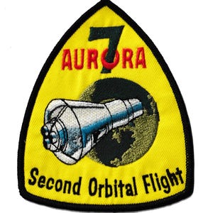 May include: Embroidered patch with a yellow background and black border. The patch features the text "7 AURORA" in red and green, and "Second Orbital Flight" in white. A detailed illustration of a spacecraft is in the centre.