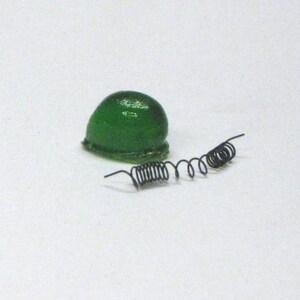 Puede incluir: Un casco de juguete de pl&aacute;stico verde con dos muelles de metal negro.