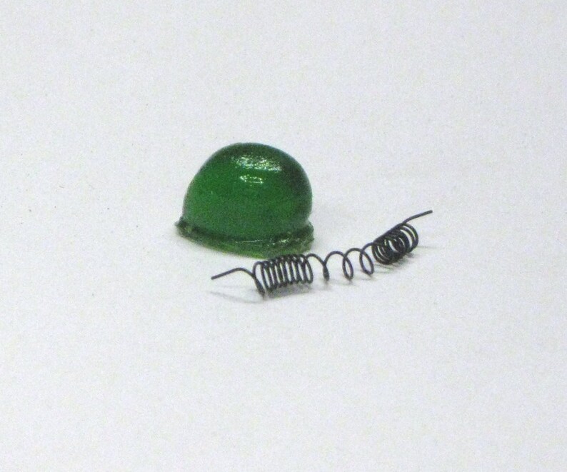 Puede incluir: Un casco de juguete de pl&aacute;stico verde con dos muelles de metal negro.