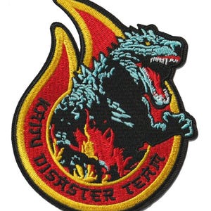 May include: Embroidered patch depicting a black monster with blue details, resembling Godzilla, inside a red and yellow flame. The patch includes the text "IRRU DISASTER TERM" in a circular arrangement around the monster.