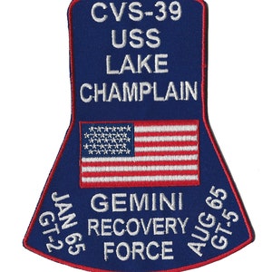 May include: A blue and red embroidered patch with the text "CVS-39 USS LAKE CHAMPLAIN GT-2 JAN 65 GEMINI RECOVERY FORCE AUG 65 GT-5" and a white American flag in the center.