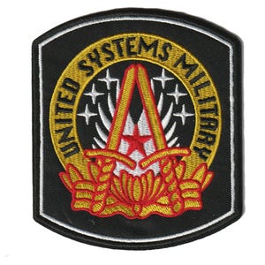 Puede incluir: Parche negro con borde blanco, con el texto dorado "UNITED SYSTEMS MILITARY". El diseño central incluye una estrella roja, detalles dorados y rojos, y un emblema floral en la parte inferior.