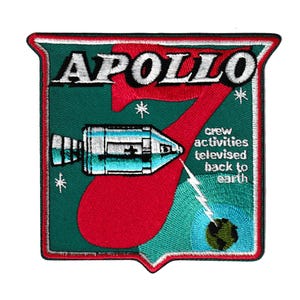 Könnte beinhalten: Gestickter Aufnäher mit dem Logo der Apollo 7 Mission. Der Aufnäher hat einen grünen Hintergrund mit dem Wort "APOLLO" in Weiß, einer großen roten "7" und einem stilisierten Raumschiff. Der Text lautet "crew activities televised back to earth".