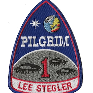 Op de afbeelding: Blauw en rood geborduurd patch met de tekst "PILGRIM 1 LEE STEGLER" en een gestileerde afbeelding van een halve maan, een ster en een planeet.