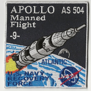 May include: Embroidered patch featuring the Apollo AS 504 mission. The patch depicts a rocket launching over a stylized Earth, with text including "Apollo Manned Flight -9-", "Atlantic", "U.S. Navy Recovery Force", and the NASA logo.