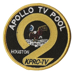 May include: A black and gold embroidered patch with the text "Apollo TV Pool Houston KPRC-TV" and a stylized eagle landing on the moon.