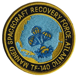 May include: Circular embroidered patch with the text "Manned Spacecraft Recovery Force, Atlantic TF-140." The patch features a blue and gold design with parachutes and a map of the Atlantic Ocean.