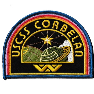 May include: Embroidered patch featuring the text "USCSS CORBELAN" in yellow, arched over a design of a planet with rings and a star. The patch has a black background with a rainbow border and a blue outer edge.