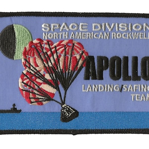 Op de afbeelding: Een blauwe en witte geborduurde patch met de tekst "SPACE DIVISION NORTH AMERICAN ROCKWELL APOLLO LANDING/SAFIN TEAM". De patch heeft een zwart en groen beeld van de maan en een rode en witte parachute.