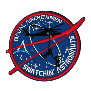 May include: Embroidered patch with a blue background, red border, and white text. The patch features a helicopter, astronauts, and the words "Naval Aircrewmen" and "Snatchin' Astronauts". A red swoosh design crosses the patch.