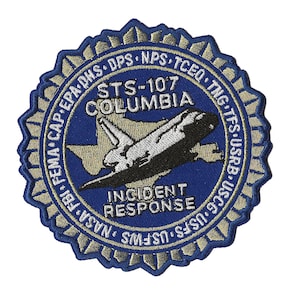 May include: A circular blue patch with gold and white embroidered details. The patch features the text "STS-107 COLUMBIA INCIDENT RESPONSE" and an image of a space shuttle over a map of Texas. The patch is surrounded by a gold border.