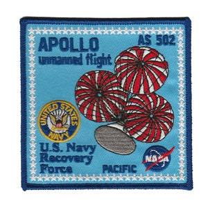 May include: A blue and white embroidered patch with the text "APOLLO unmanned flight AS 502" and a graphic of a spacecraft with three parachutes. The patch also includes the text "U.S. Navy Recovery Force PACIFIC" and the NASA logo.