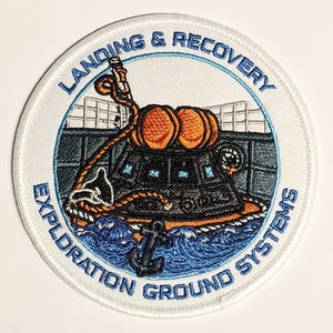 May include: Embroidered patch with a circular design. The patch features the text "LANDING & RECOVERY EXPLORATION GROUND SYSTEMS" in blue. The central image depicts a spacecraft with orange spheres, a rope, and an anchor, set against a blue and white background.