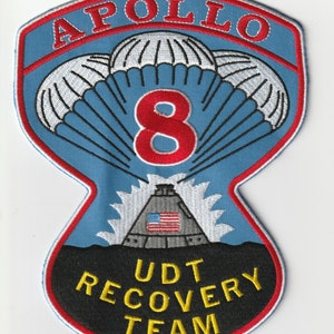 Pode incluir: Um remendo bordado azul e vermelho com o texto "APOLLO 8 UDT RECOVERY TEAM" e uma representação de uma nave espacial com três paraquedas e o número "8" em vermelho.
