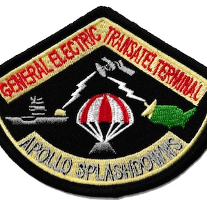 May include: Embroidered patch with a black background and a yellow border. The patch features text that reads "GENERAL ELECTRIC TRANSATEL TERMINAL" and "APOLLO SPLASHDOWNS". The design includes a parachute, a satellite, and a map of the United States.