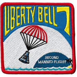 May include: Embroidered patch with a red border, featuring the text "LIBERTY BELL 7" in yellow on a blue background. A red and white parachute design is centered, with the text "SECOND MANNED FLIGHT" below. The patch has a white background with a blue wave design at the bottom.