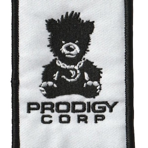 May include: A rectangular patch with a black border and a white background. The patch features a black teddy bear design wearing a chain, with the words "PRODIGY CORP" in black letters below the bear.