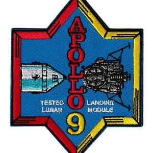 May include: A blue, star-shaped patch featuring the text "APOLLO 9" in red, with a white and teal lunar module and a black landing module. The patch also includes the words "TESTED LUNAR" and "LANDING MODULE".