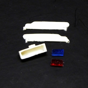 May include: Three white plastic pieces for a model car, including a roof, a rear window, and a light bar. Two red and blue plastic pieces are also included.