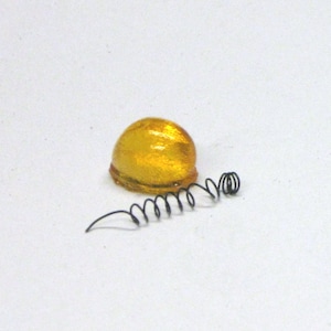 May include: A clear amber colored glass dome with a black metal spring attached to it.