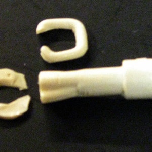 May include: Three white plastic pieces for a model kit. The pieces are a long tube with a rounded end, and two curved pieces that look like a horseshoe.