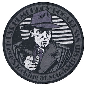 May include: Embroidered patch featuring a stylized image of Humphrey Bogart in a fedora and trench coat, holding a gun. The patch is circular with text that reads "Here's looking at you, kid!" in a circular pattern around the image.