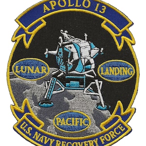 May include: A black and gold embroidered patch with the text "Apollo 13 U.S. Navy Recovery Force" and a depiction of a lunar module landing on the moon. The patch also includes the text "Lunar Landing Pacific".