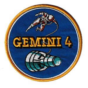May include: Embroidered patch featuring the Gemini 4 mission. The design includes an astronaut in a spacesuit tethered to a spacecraft, with the words "GEMINI 4" in gold lettering. The patch has a blue background with a gold border.