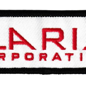 May include: Embroidered patch with the text "ILARIA CORPORATION" in red on a white background. The patch has a black border and is rectangular in shape. The text is in a bold, sans-serif font.
