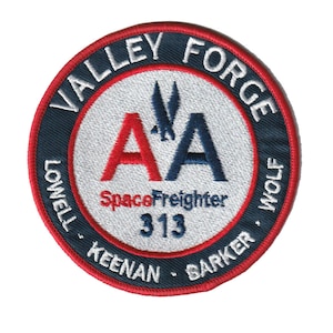 Puede incluir: Un parche redondo bordado en azul y rojo con el texto "Valley Forge" y "Lowell Keenan Barker Wolf" alrededor del exterior. El centro del parche presenta las letras "A" y "A" en rojo y azul, con el texto "Space Freighter 313" debajo.
