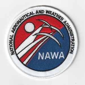 May include: A circular embroidered patch featuring a red and blue background divided diagonally. It displays a white sun, three white swooping lines, and the text "NATIONAL AERONAUTICAL AND WEATHER ADMINISTRATION" along the border with "NAWA" in the center.