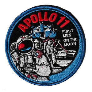 May include: Circular embroidered patch commemorating the Apollo 17 mission. The design shows an astronaut, lunar module, and the text "APOLLO 17" in red, with "FIRST MEN ON THE MOON" in white. The patch has a black centre with a blue border.