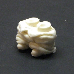 May include: A white ceramic sculpture of two figures with their arms intertwined. The sculpture is abstract and has a smooth, rounded surface.