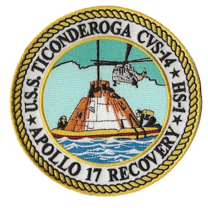 Op de afbeelding: Een ronde geborduurde patch met een gouden touwrand. Het midden toont een witte en oranje Apollo 17 reddingscapsule die door een helikopter wordt opgetild. De tekst rond de rand luidt "USS TICONDEROGA CVS 14 * HS-1 * APOLLO 17 RECOVERY".