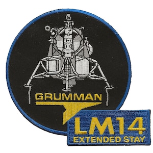 May include: A black and white embroidered patch of a lunar module with the text "Grumman" below it. A blue and yellow embroidered patch with the text "LM14 Extended Stay" is below the lunar module patch.